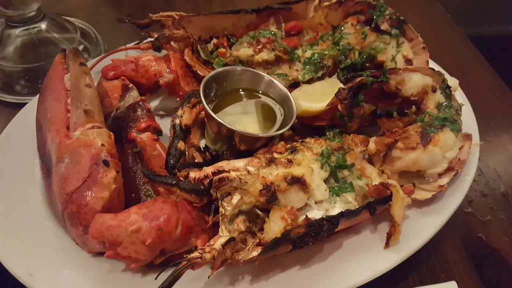 Split grilled lobster with melted cheese, green herbs, lemon, and butter.