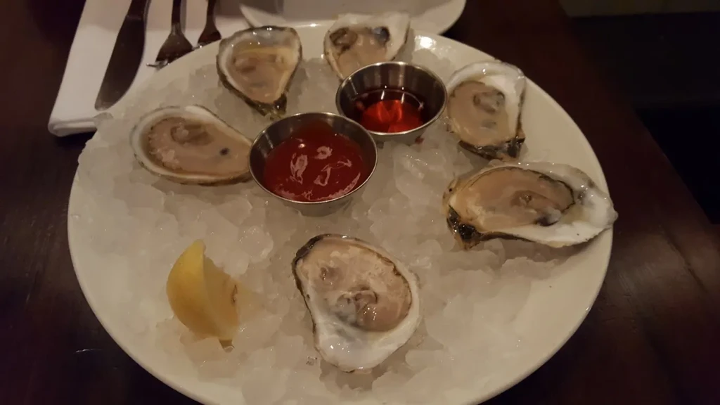 Seven freshly shucked oysters on ice with two sauces and lemon.