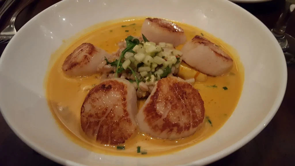 Close-up of five pan-seared scallops, grain, green relish, orange sauce.