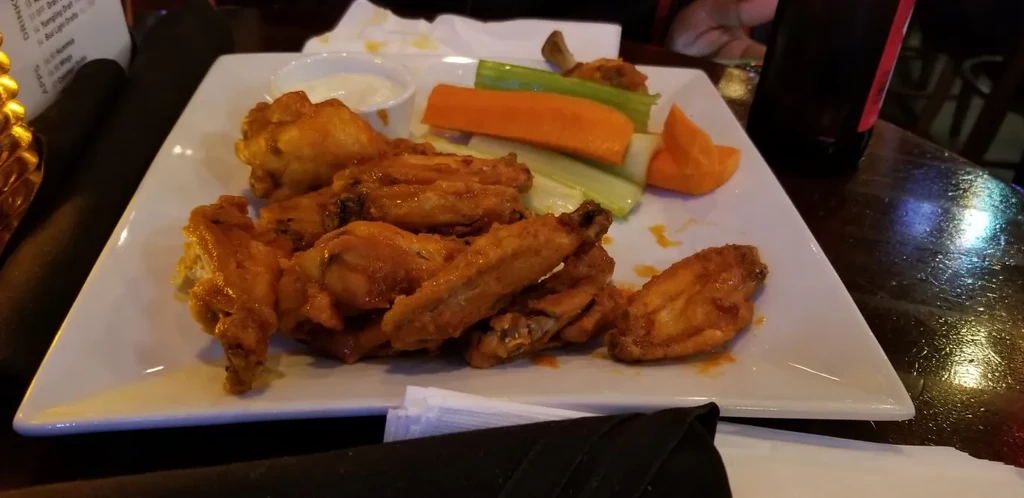 Plate of glossy orange buffalo wings, dipping sauce, and vegetables.