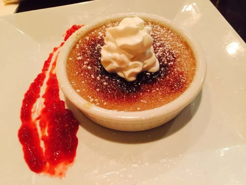 Crème brûlée with caramelized top, whipped cream, and berry coulis.