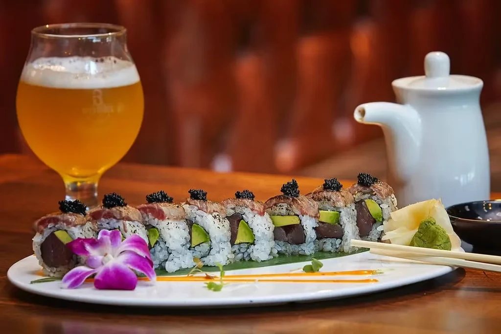 Sushi rolls with beef, caviar, avocado, beer, and sauce on a plate.