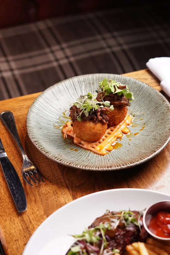 Two fried arancini with pulled meat and microgreens on a plate.