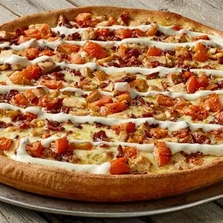Round chicken and bacon pizza with orange chunks and white sauce drizzle.