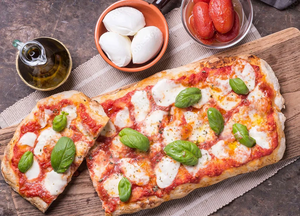 Long rectangular pizza Margherita with fresh basil, mozzarella, and tomatoes.