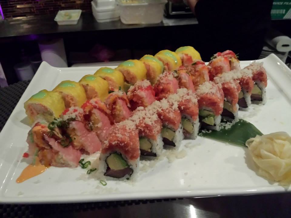 Assortment of yellow and pink sushi rolls on a long white plate.
