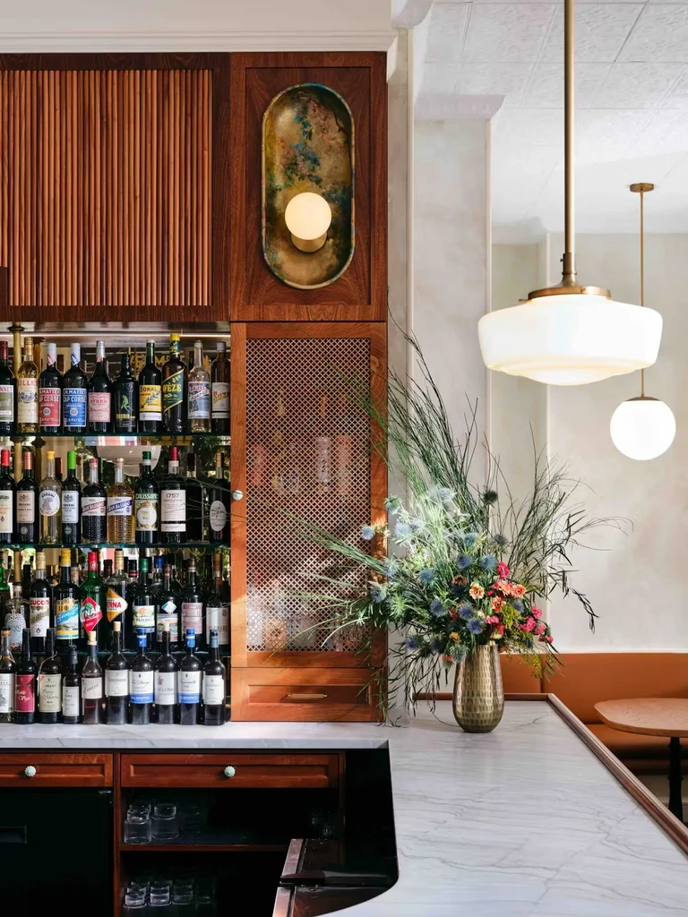 Restaurant bar interior with liquor bottles, marble counter, and floral arrangement.