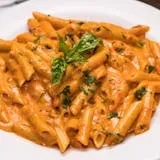 Penne pasta with orange sauce, basil leaves, and parsley on white plate.