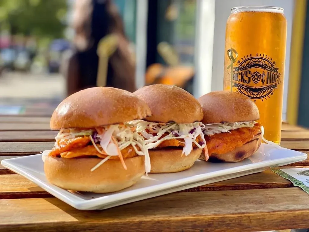Three chicken sliders with coleslaw and a beer on a wooden table.