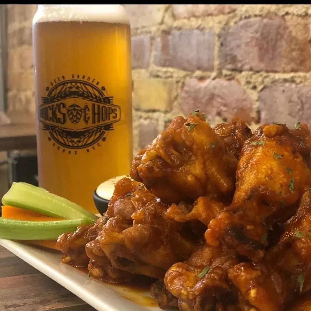 A glass of beer with wings, celery, and carrots on a plate.