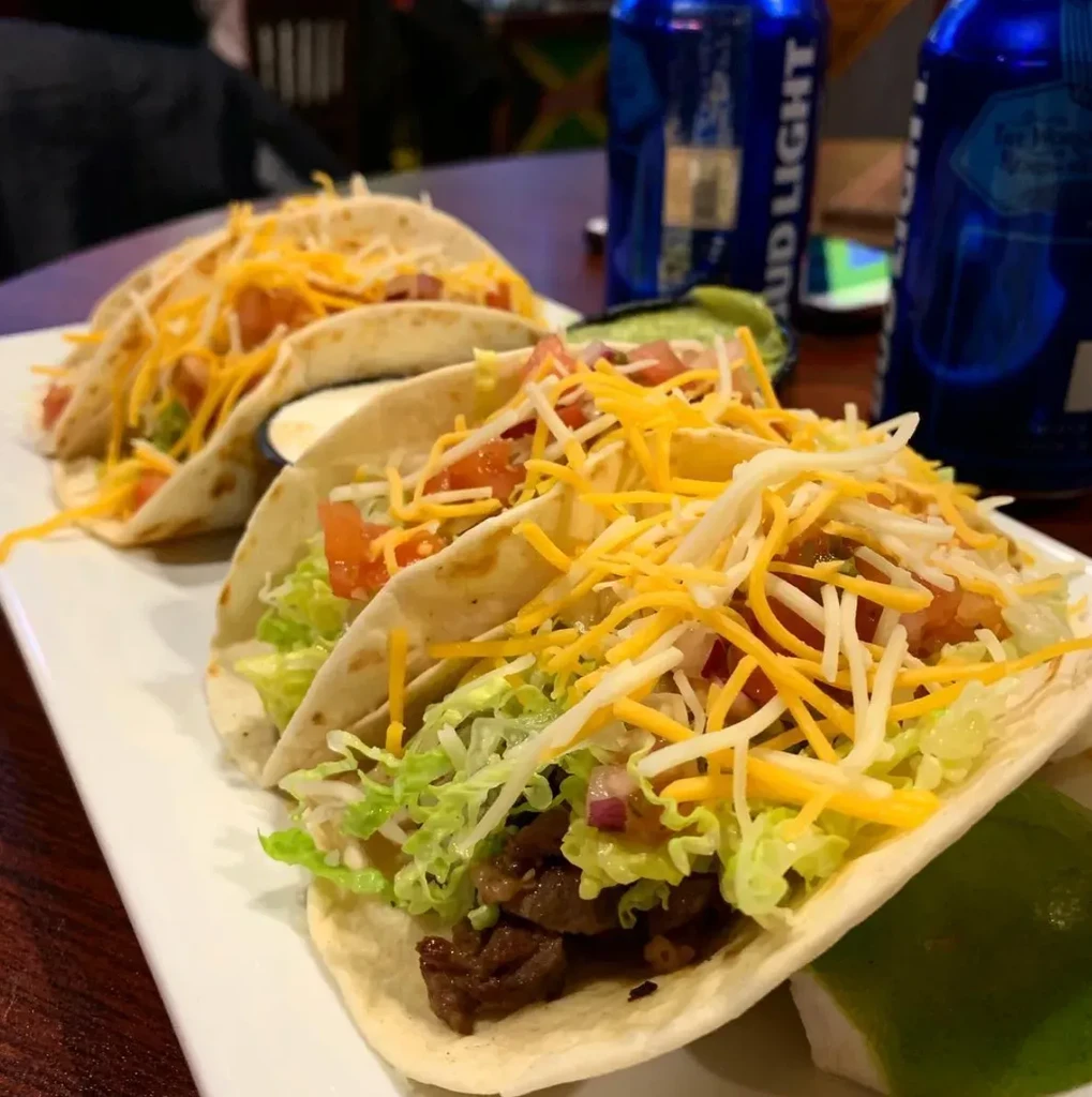 Three tacos with meat, lettuce, cheese, and tomatoes on a white plate.