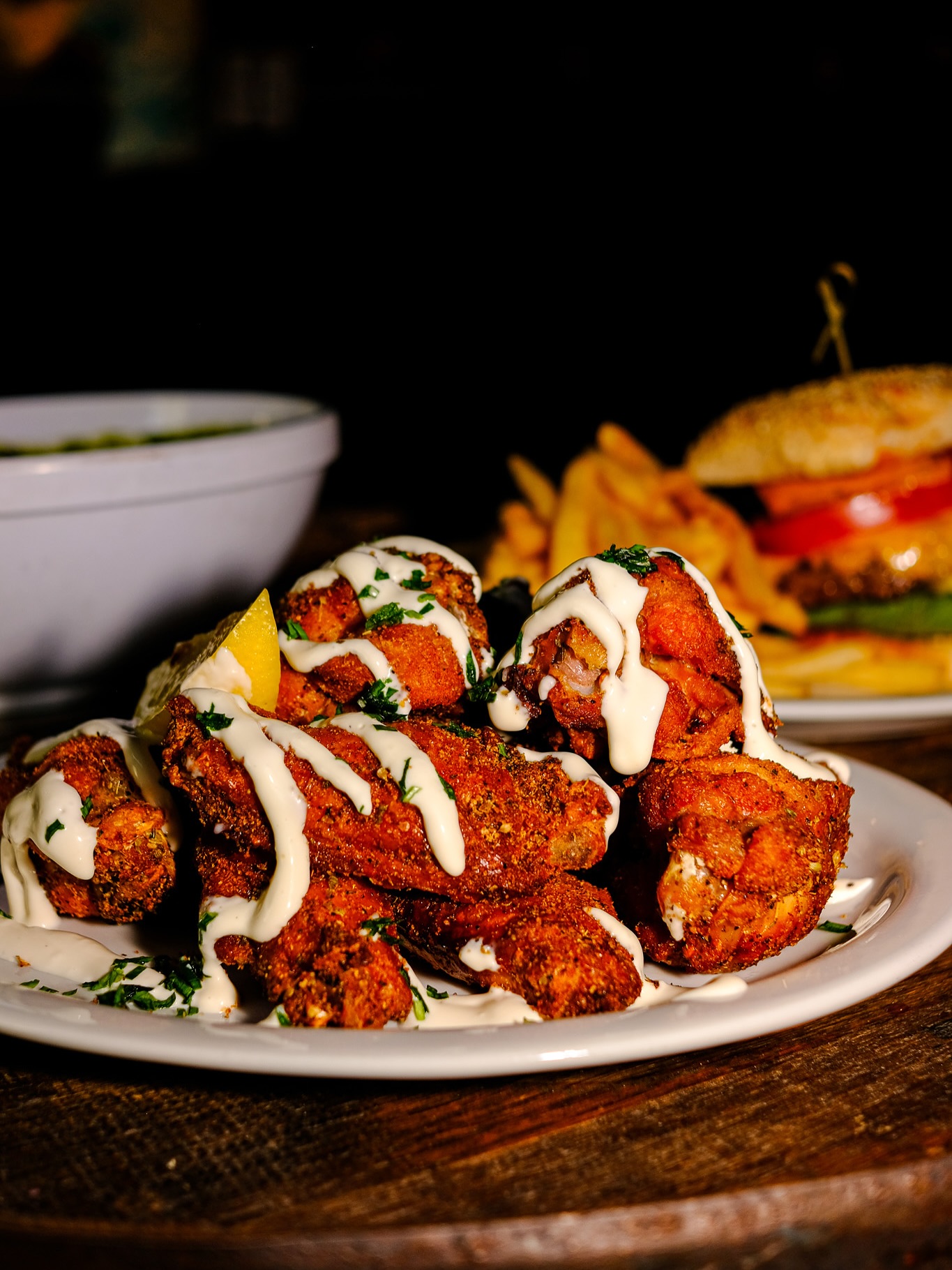 Plate of fried chicken wings, drizzled with white sauce and lemon.