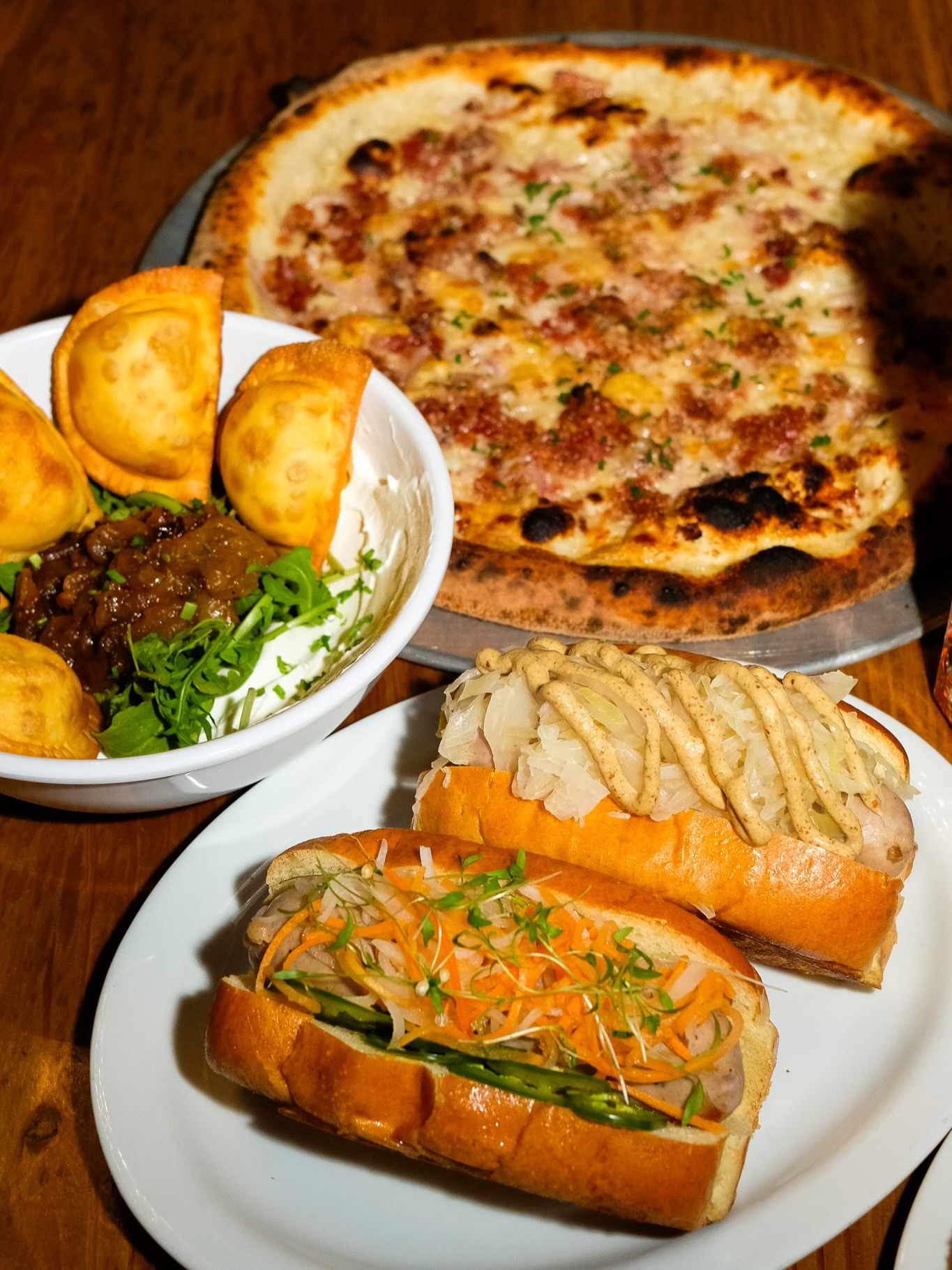 Various dishes: pizza, empanadas, and hot dogs on a wooden table.