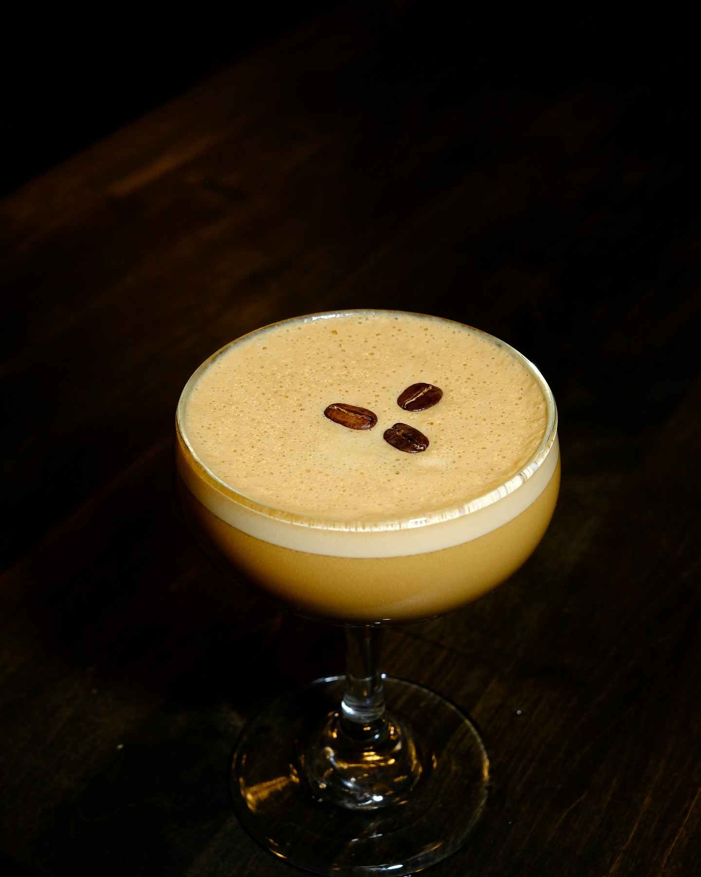 A frothy espresso martini garnished with three coffee beans on a dark background.