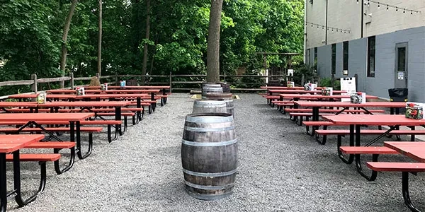 Outdoor dining area with red picnic tables, trees, and whiskey barrels.