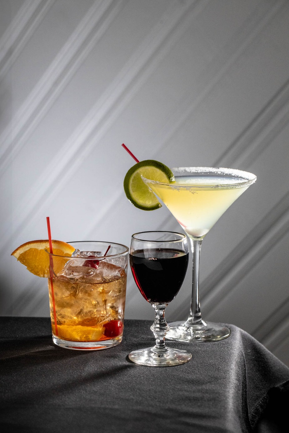 Three drinks: iced cocktail, red wine, and a garnished martini.