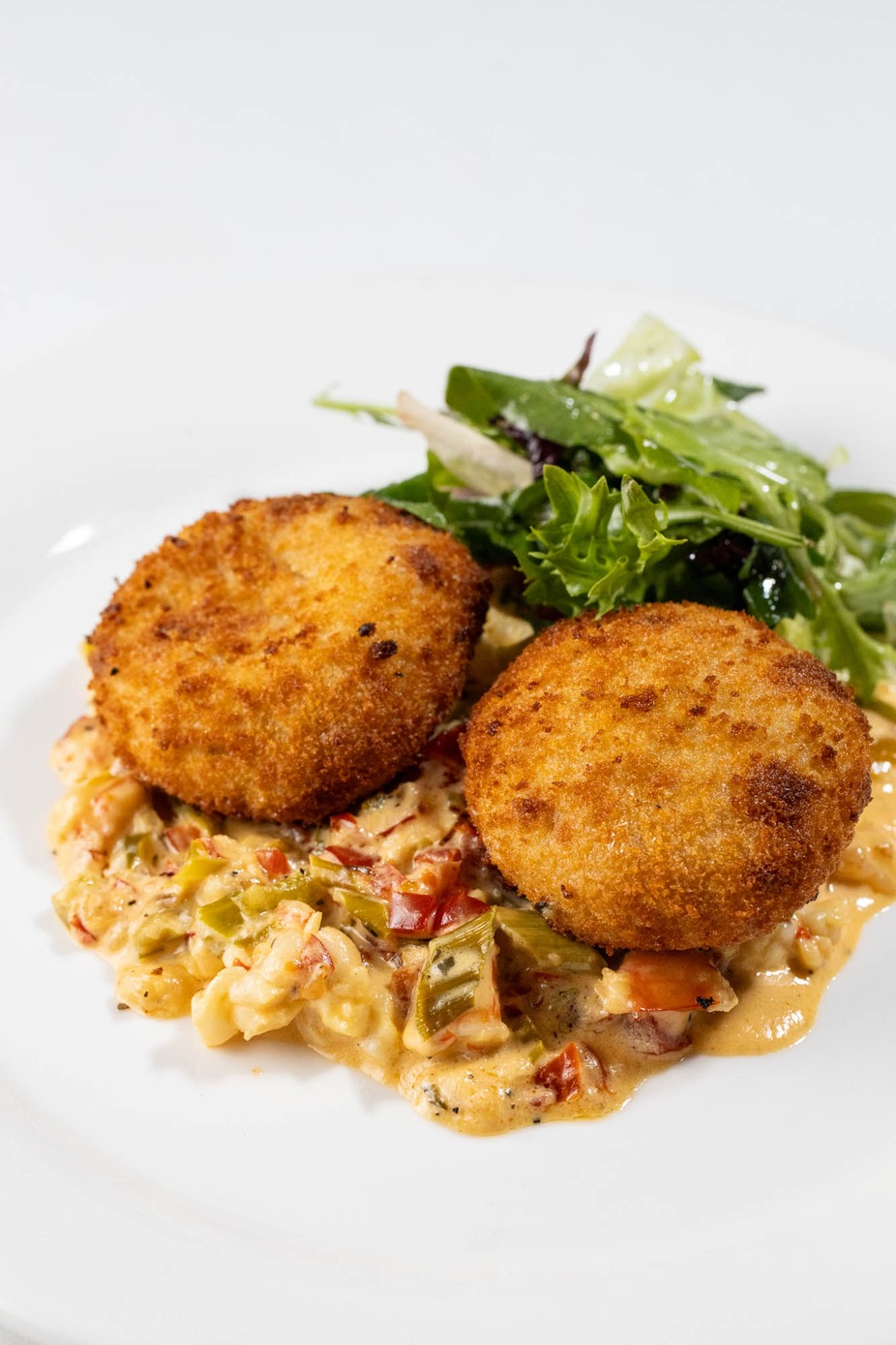 Two golden-brown patties on creamy sauce with vegetables, side salad.