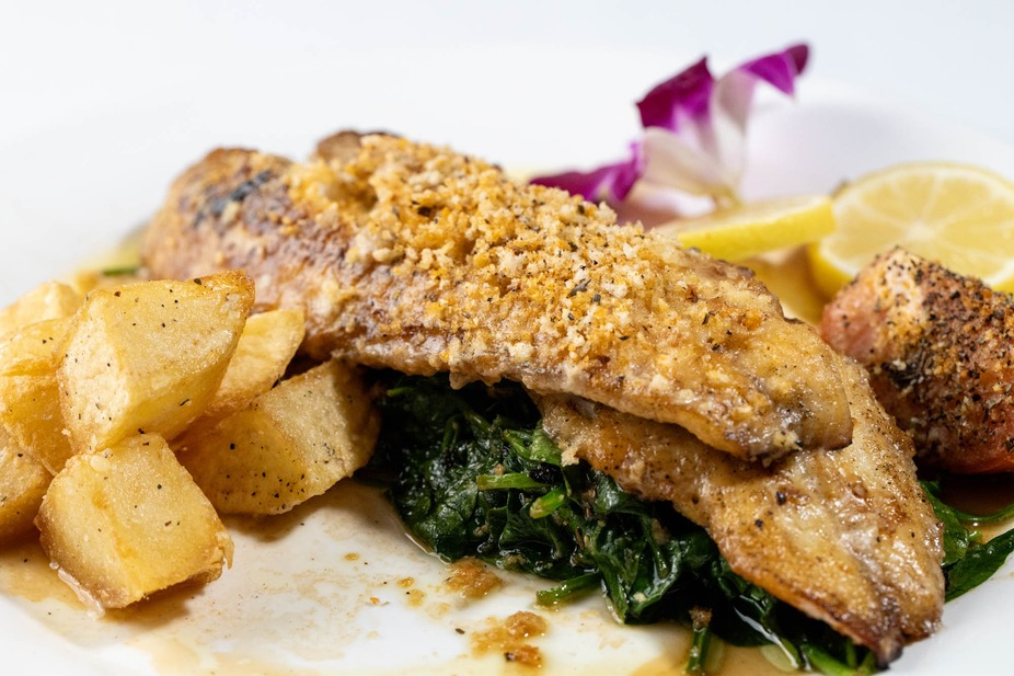 Crusted fish fillets, spinach, roasted potatoes, lemon, and flower garnish.