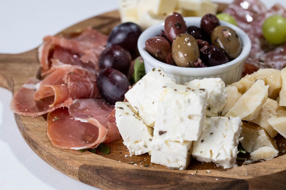 A wooden board of cured meats, various cheeses, olives, and grapes.