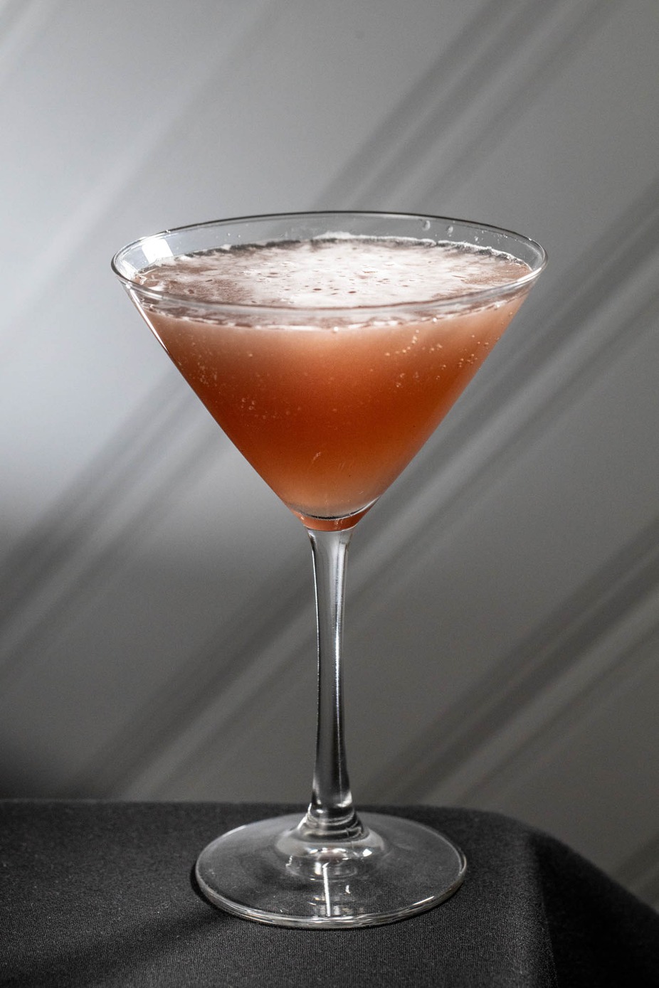 Martini glass with a bubbly, reddish-pink cocktail.