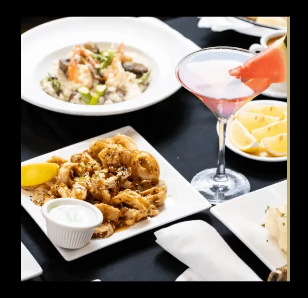 Fried calamari, pink cocktail, and pasta dish on a restaurant table.