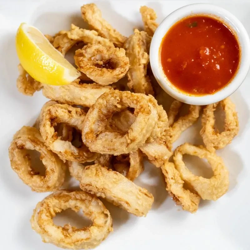 Plate of crispy fried calamari, lemon wedge, and red dipping sauce.