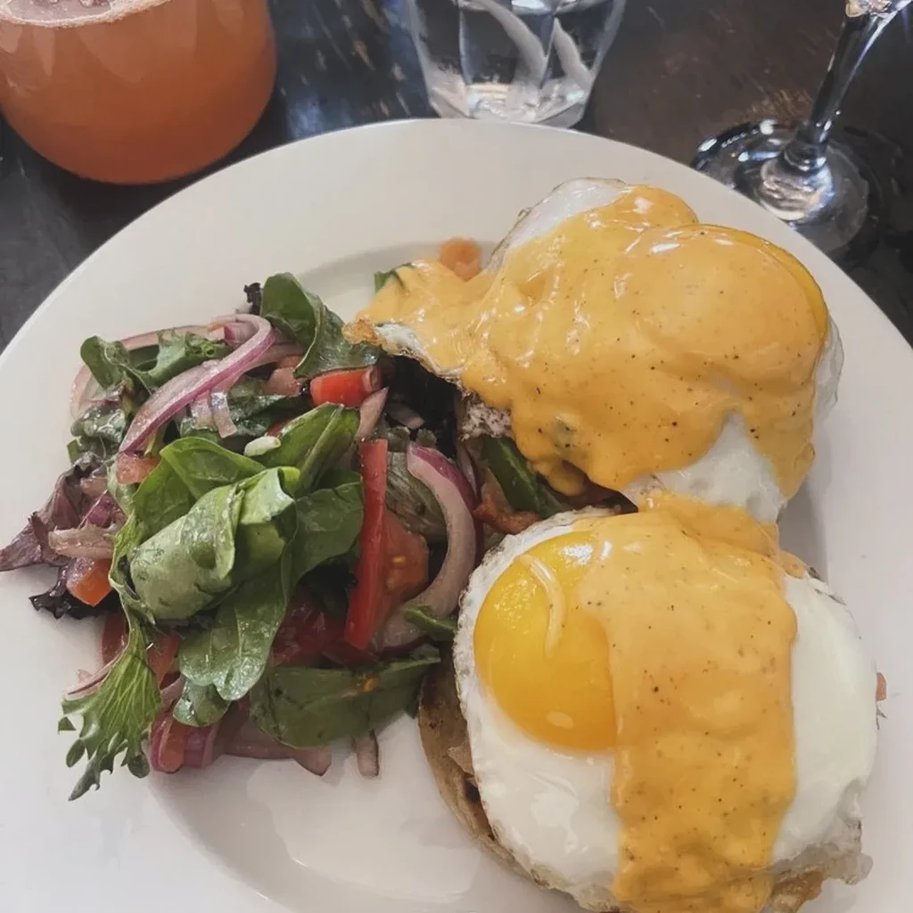 Two eggs Benedict with hollandaise sauce and a side salad.