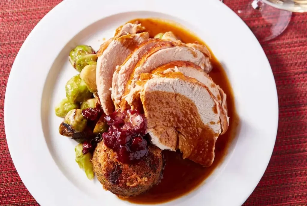 Plate of sliced turkey, gravy, cranberry sauce, stuffing, and Brussels sprouts.