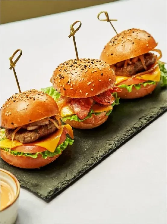 Three mini burgers on a black slate platter with dipping sauce.