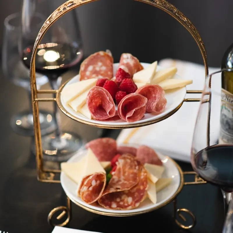 A two-tier stand holds plates of charcuterie, cheese, and raspberries.