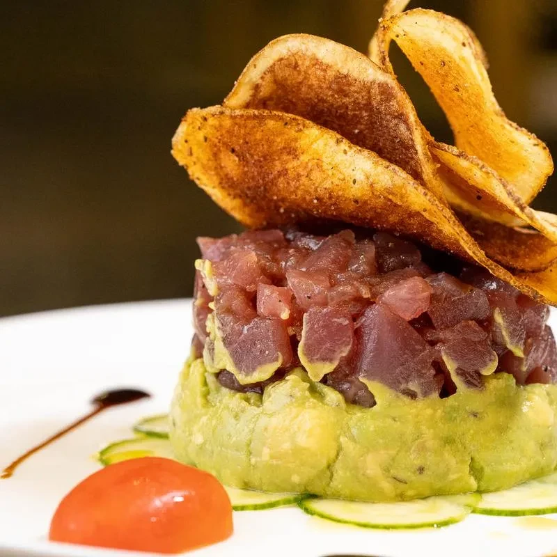 Tuna tartare with avocado and potato chips on a white plate.