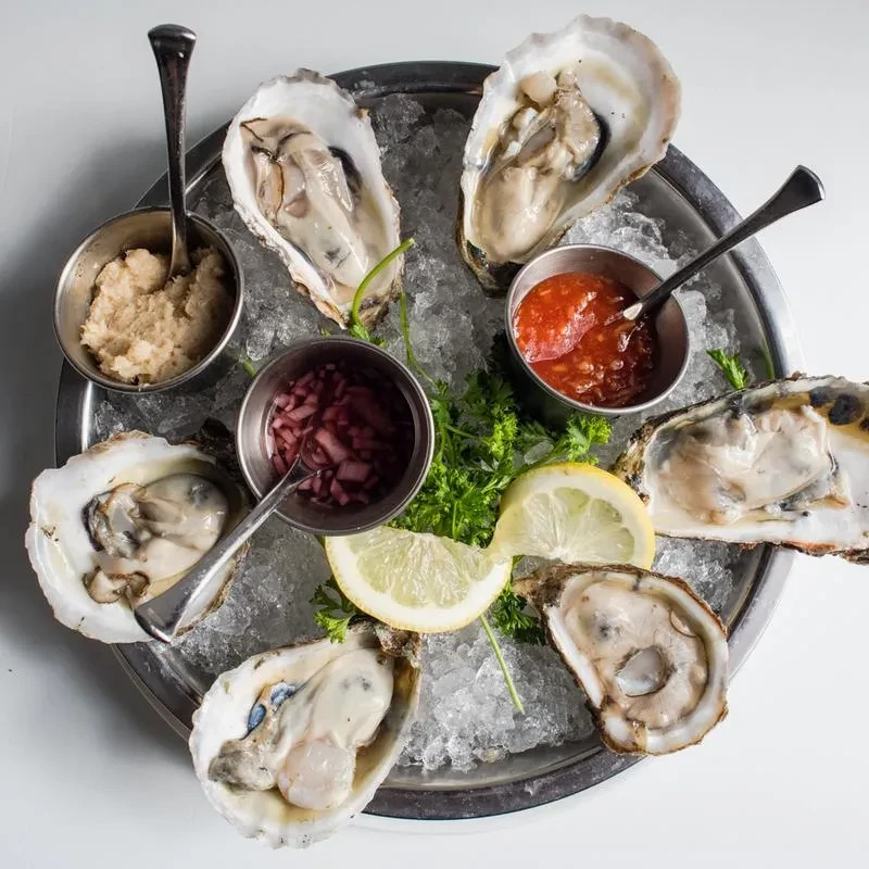 Six oysters on a bed of ice with sauces and lemon wedges.