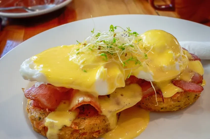 Eggs Benedict with bacon and sprouts on a white plate.
