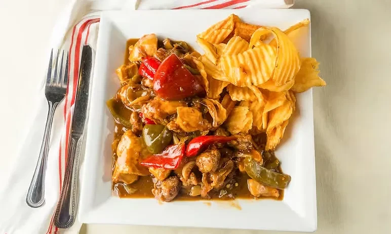 A plate of sweet and sour chicken with bell peppers and potato chips.