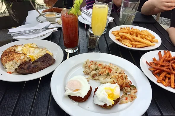A table laden with breakfast dishes: hash browns, eggs, steak, and fries.