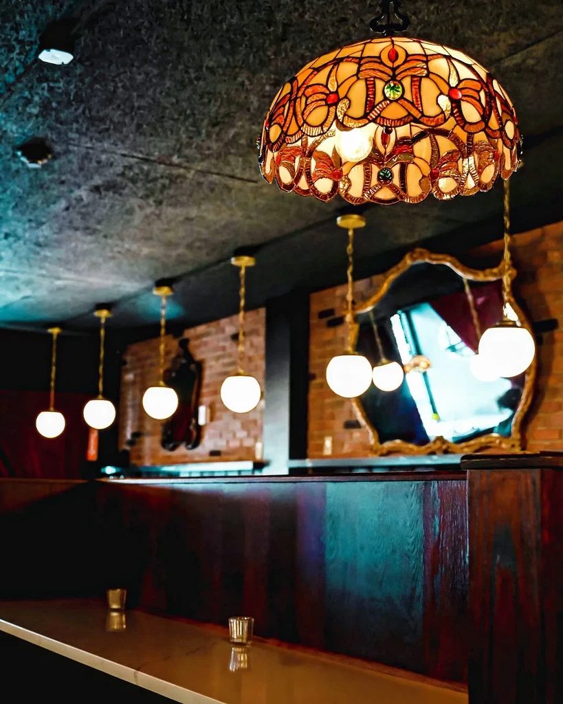 A stained-glass Tiffany lamp hangs above an empty bar with other pendant lights.