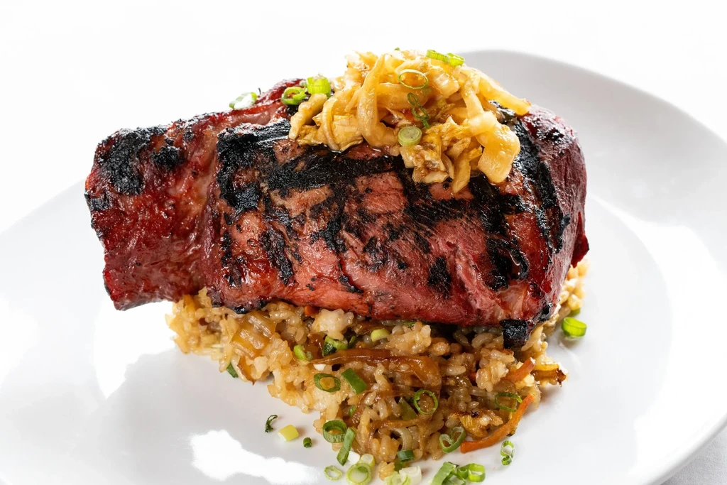 Grilled steak with scallions on a bed of rice on a white plate.
