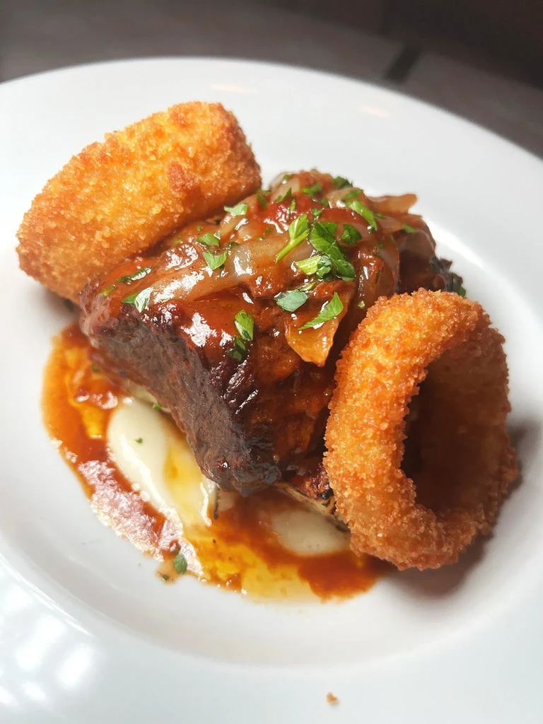 Short ribs with gravy, mashed potatoes, and fried onion rings.