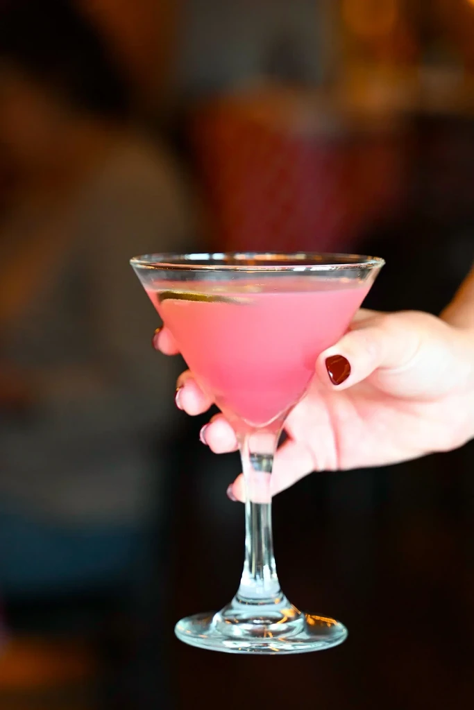 A hand holding a martini glass filled with a pink drink.