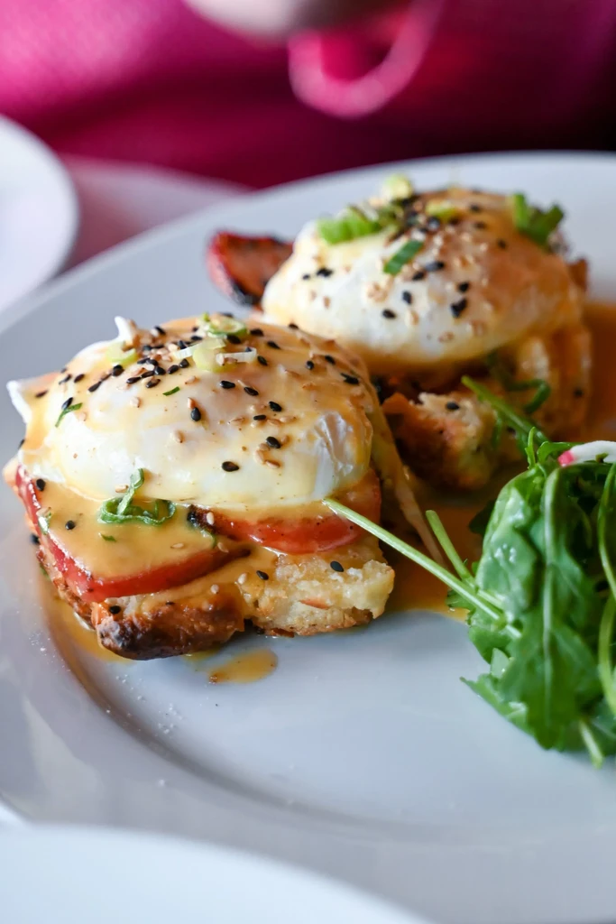 Two gourmet egg dishes with sauce, sesame seeds, and greens on a white plate.