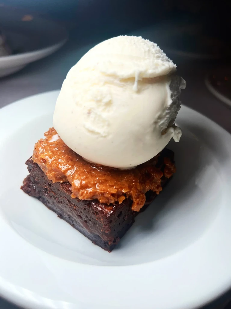 Brownie with caramel topping and a scoop of vanilla ice cream.
