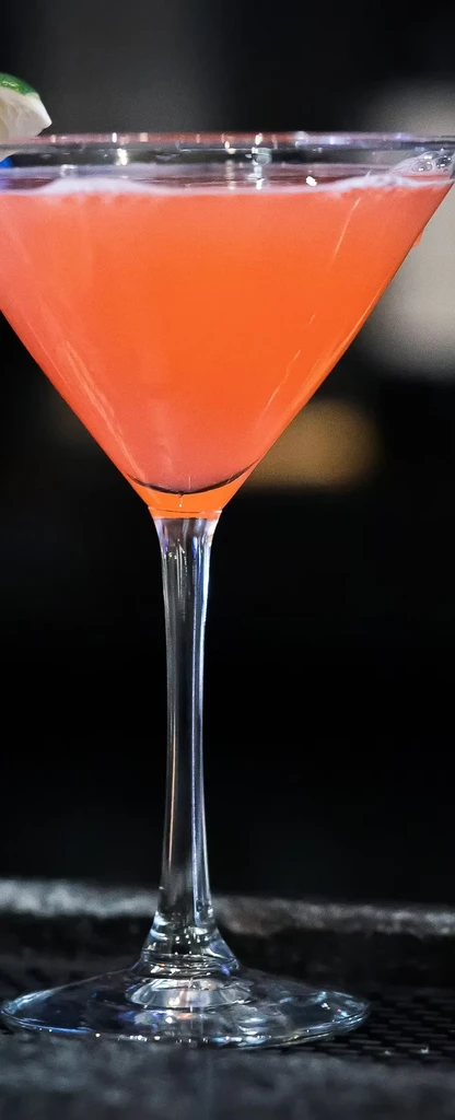A cocktail with orange liquid and a lime wedge in a martini glass.
