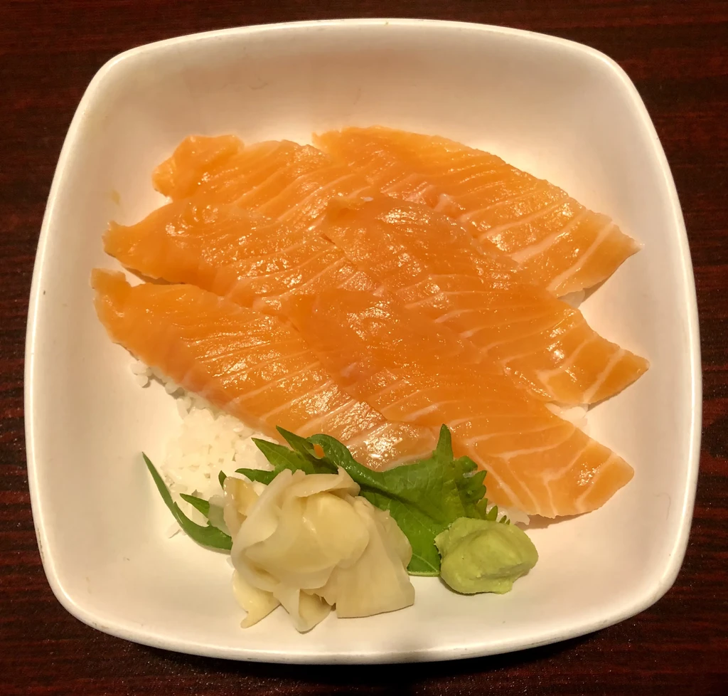 Slices of salmon sashimi over rice with ginger and wasabi.