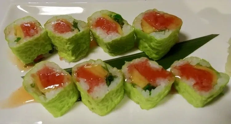 Eight lettuce-wrapped sushi rolls with tuna and mango on a white plate.