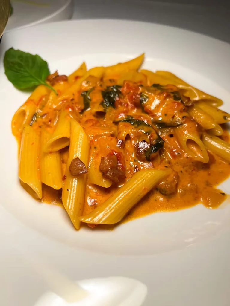 Penne pasta in a creamy red sauce with green and brown ingredients.