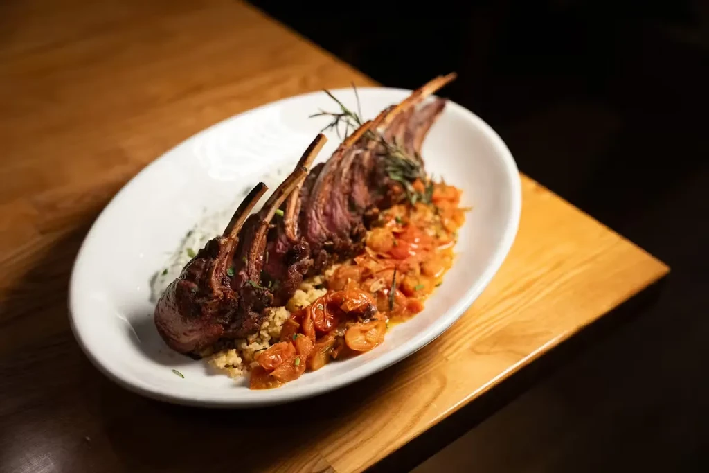 A plate of rack of lamb with bulgur and stewed tomatoes.