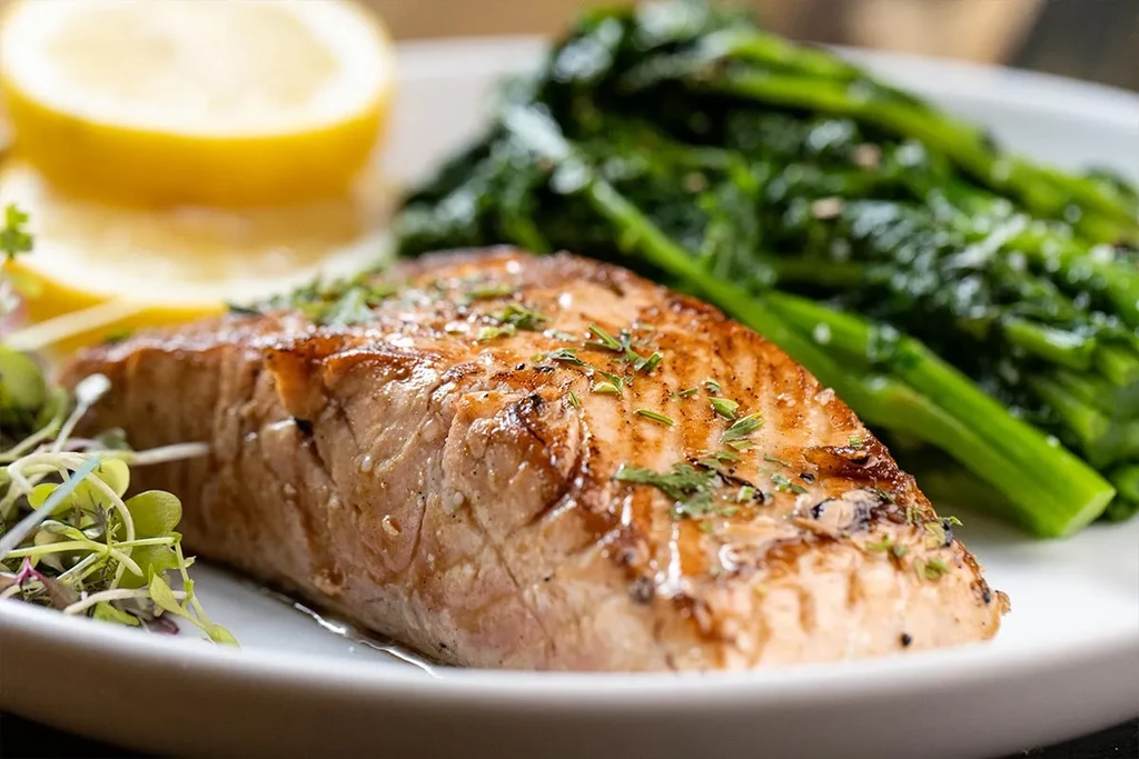 A close-up of seared salmon with broccoli rabe and lemon wedges.