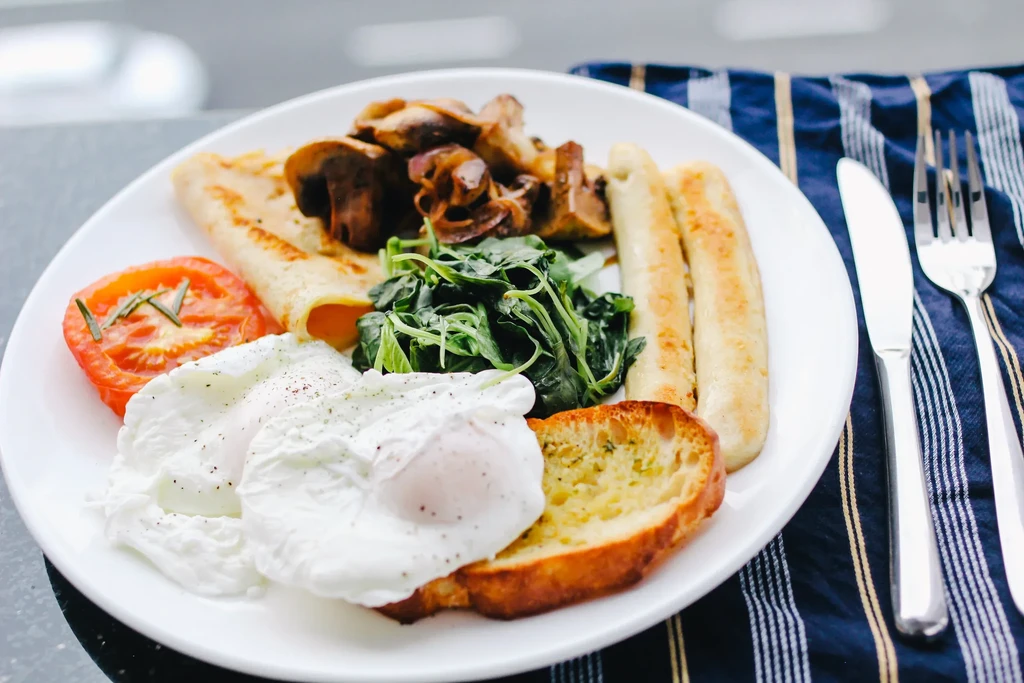 A full breakfast plate with eggs, bread, mushrooms, spinach, tomato, and sausages.