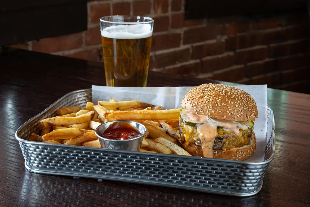 A basket of fries, ketchup, a cheesy burger, and a glass of beer.