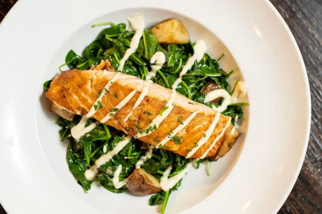 Seared salmon with spinach, potatoes, and white sauce in a white bowl.